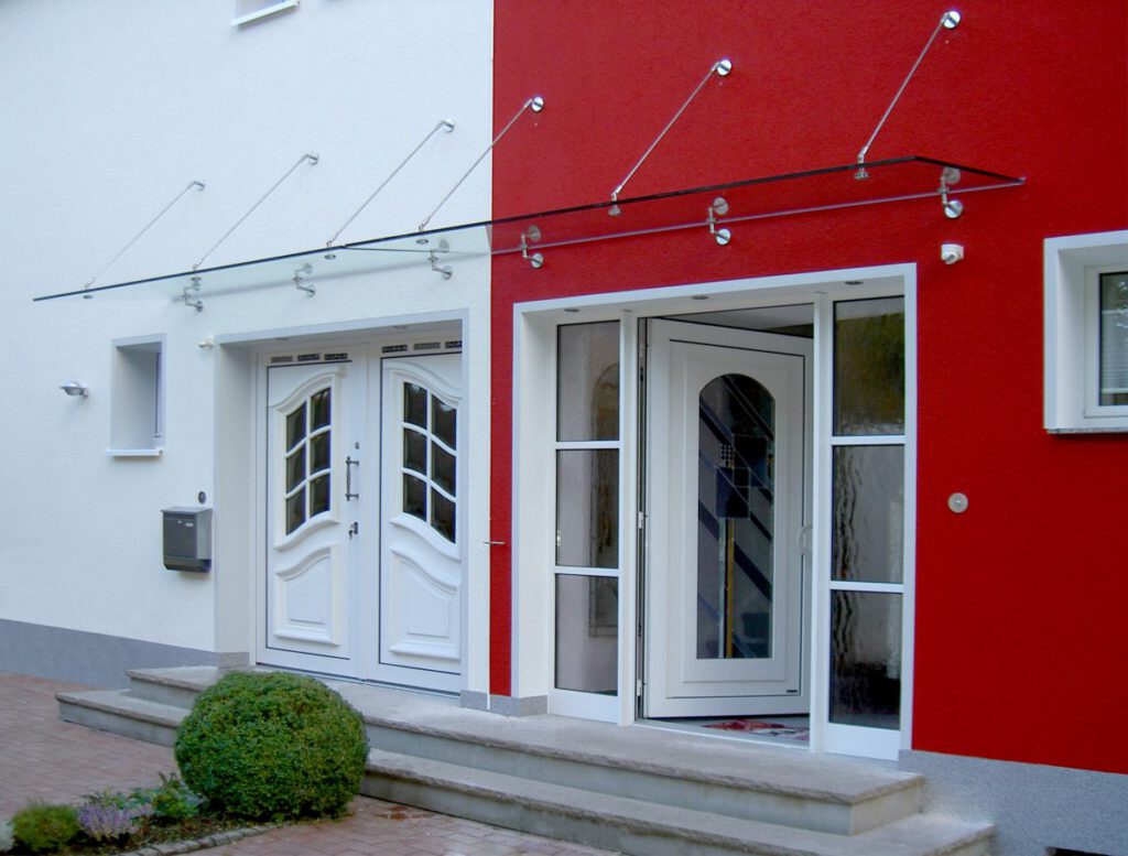 Weiße Doppelflügel-Haustür mit Ornamentglas unter einem Glasvordach von Panther